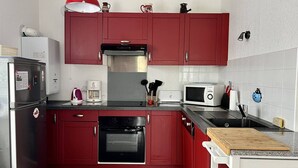 A compact kitchen with red cabinets, a stainless steel refrigerator, a microwave, a coffee maker, and a wooden cutting board on the countertop. - Central T2 Apartment with Terrace, Cambo-les-Bains (Cambo-les-Bains)