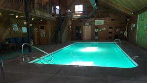 Una piscina interior con revestimiento de madera, una escalera y señales de seguridad.