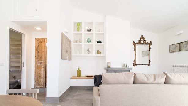 Un soggiorno moderno con un divano beige, un tavolo da pranzo in legno e una parete bianca con mensole che espongono oggetti decorativi.