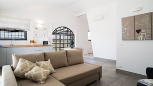 Un soggiorno moderno con un divano modulare beige, un'area pranzo con un tavolo rotondo e una cucina con finestra e porta decorativa.
