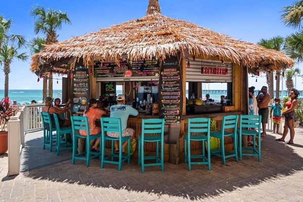 Un bar situé en bord de mer, doté d’un toit de chaume, de tables en plein air et d’un tableau affichant le menu.