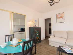 A dining area with a table set for two, a cabinet with a floral design, a sofa, and a framed certificate on the wall.