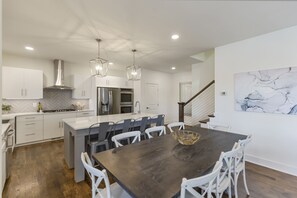 A modern kitchen with white cabinetry, a central island, stainless steel appliances, and a dark wooden dining table with white chairs. - Perfect Lake Hartwell Getaway - Gorgeous Lake Views! (Seneca)