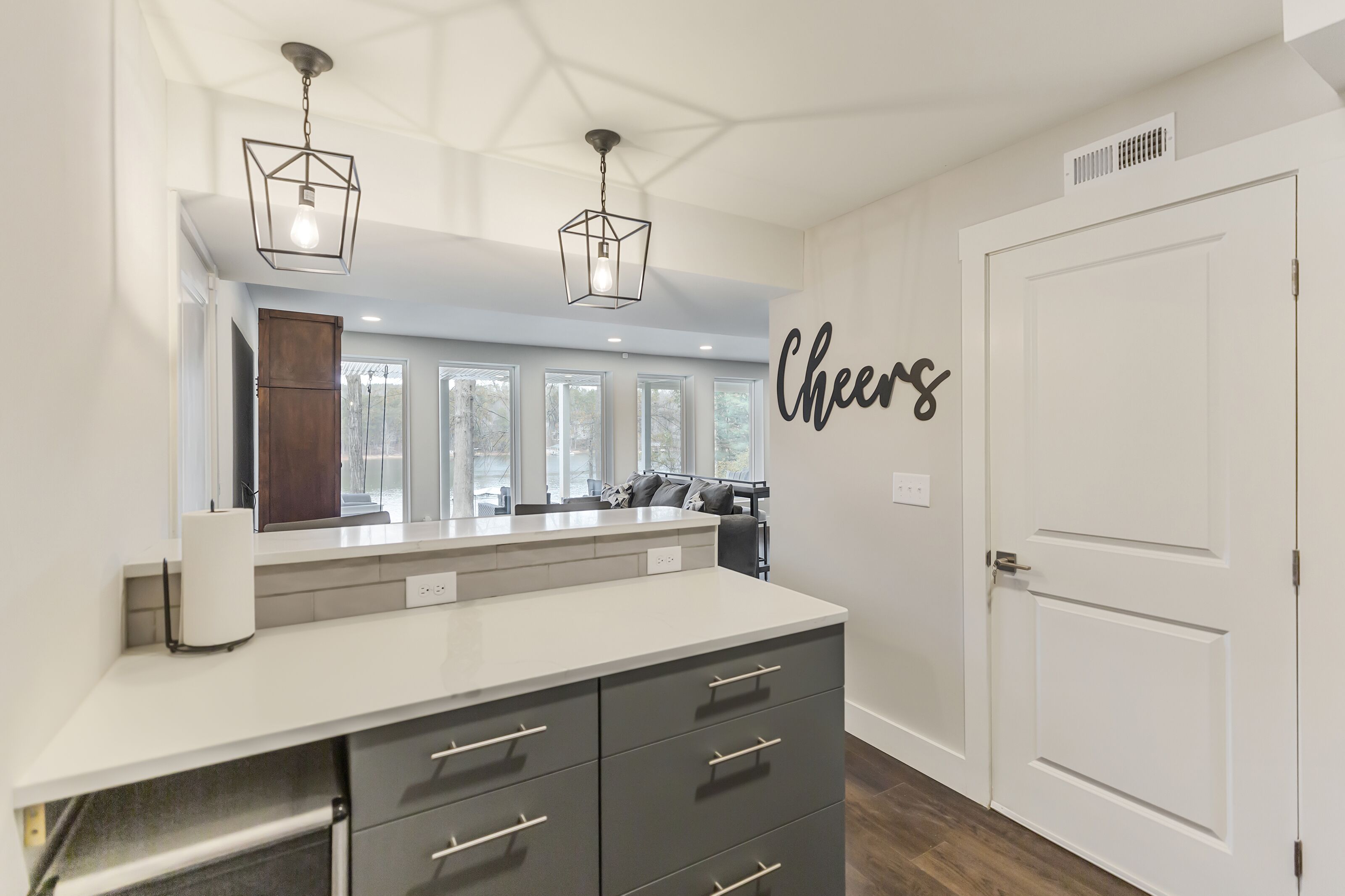 A modern kitchen with a large island, pendant lights, and a 'Cheers' wall decal.