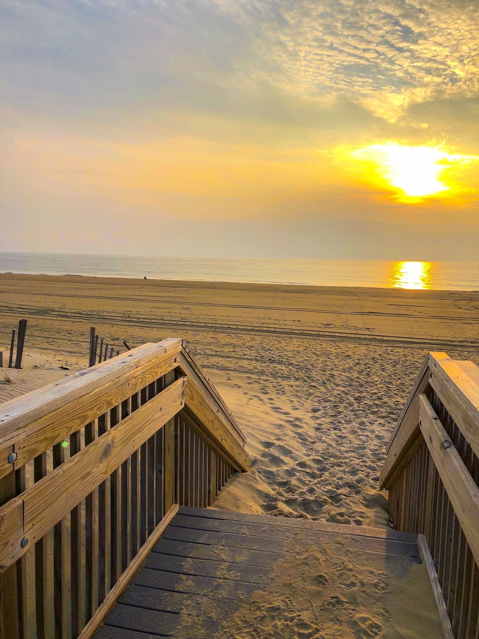 A wooden boardwalk leading to a beach with a sunset in the background.