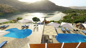 Zona de piscina con sillones de descanso y sombrillas, con vistas a un lago y montañas.