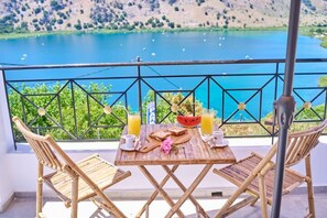 A wooden table with a breakfast setup on a balcony overlooking a lake.