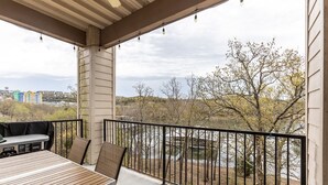 A covered balcony with a table and chairs, overlooking a river and trees.