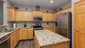A kitchen with wooden cabinets, granite countertops, stainless steel appliances, and a decorative tree wall art piece.