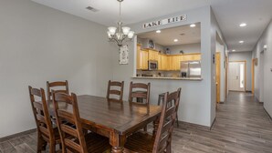 A dining area with a wooden table and chairs, a chandelier, and a kitchen visible through an archway with a sign reading "LAKE LIFE".