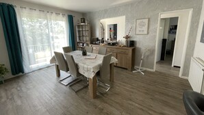 Un'area pranzo con un tavolo imbandito per quattro persone, un mobiletto in legno con vetrine e vista all'esterno tramite una grande finestra.