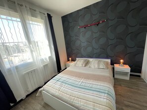 A bedroom with a bed, two bedside tables with lamps, a window with curtains, and a patterned wall.