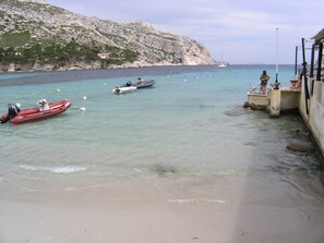 A beach with boats, a rocky cliff, and a small building.