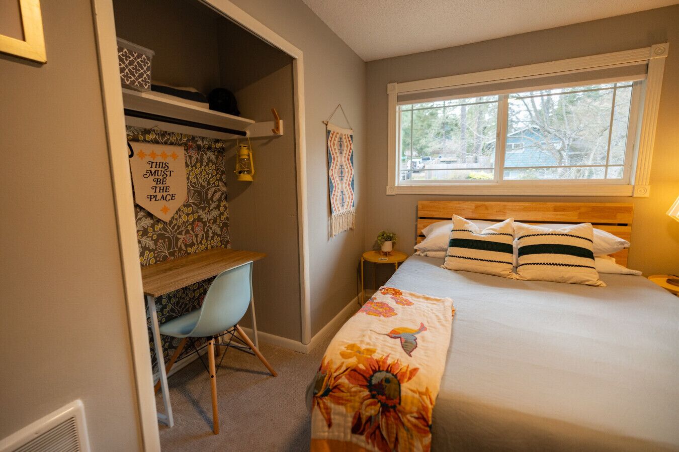 Een slaapkamer met een bed, een bureau, een stoel, een raam en een muur met een decoratief bord.