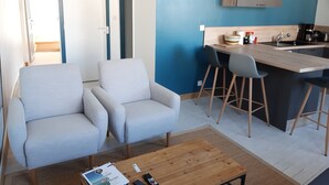 A modern living room with two grey sofas, a wooden coffee table, and a kitchen area with a bar counter, stools, and a microwave.
