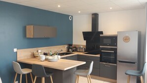 A modern kitchen with a wooden countertop, bar stools, a built-in oven, and a refrigerator.