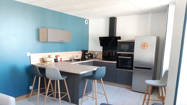 A modern kitchen with a central island, bar stools, a built-in oven, and a refrigerator.