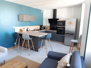 Une cuisine moderne dotée d’un îlot central, de tabourets de bar, d’un four encastré et d’un réfrigérateur.