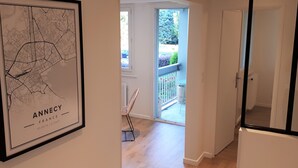 A hallway with a framed map of Annecy, France, a chair, and a sliding glass door leading to an outdoor area with a balcony.