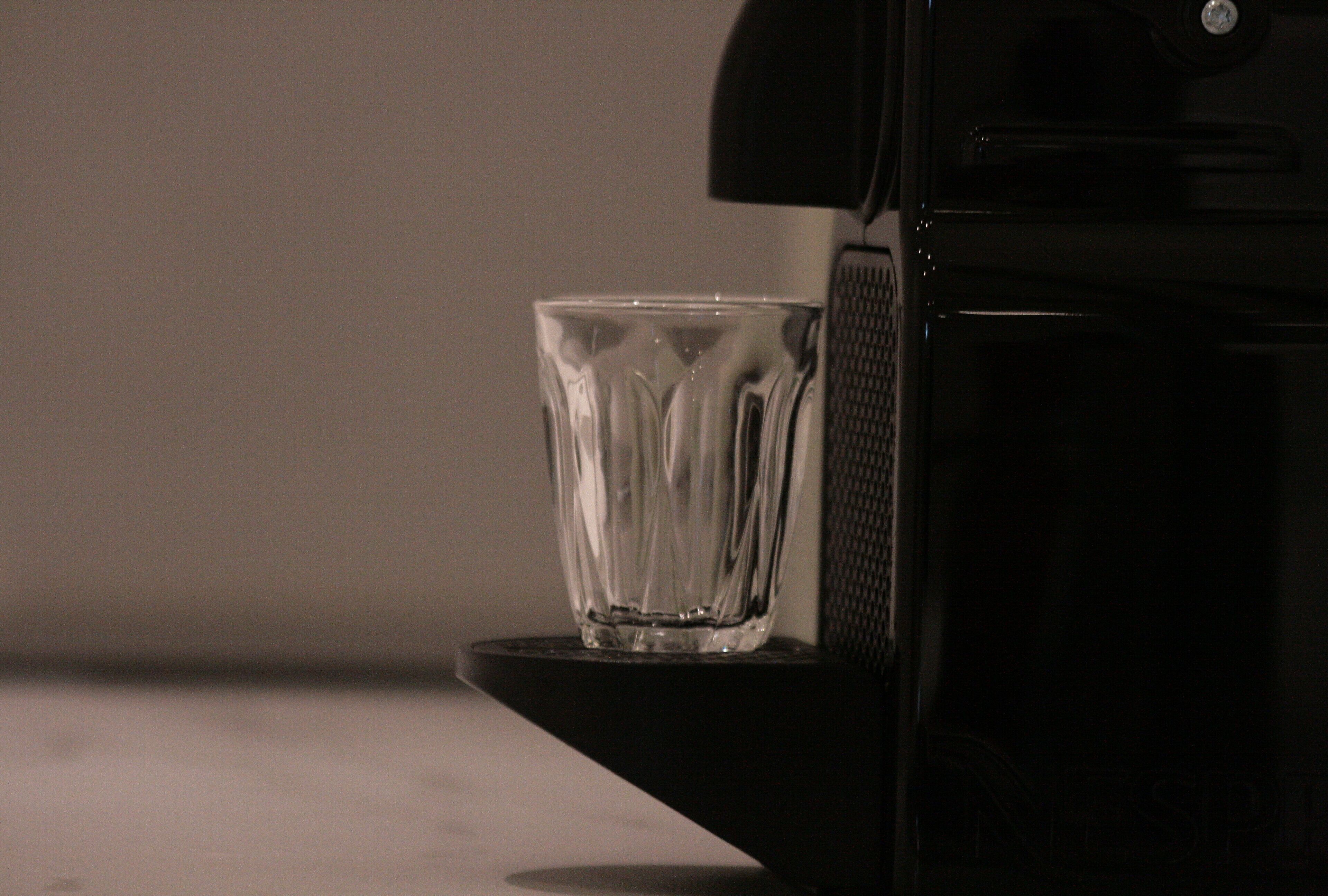 Una taza de vidrio transparente sobre una superficie negra, junto a un electrodoméstico negro, posiblemente una cafetera.