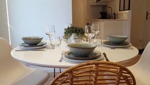 A round dining table set with bowls, plates, and cutlery. There are two white chairs and a wicker chair. A small plant is on the table.