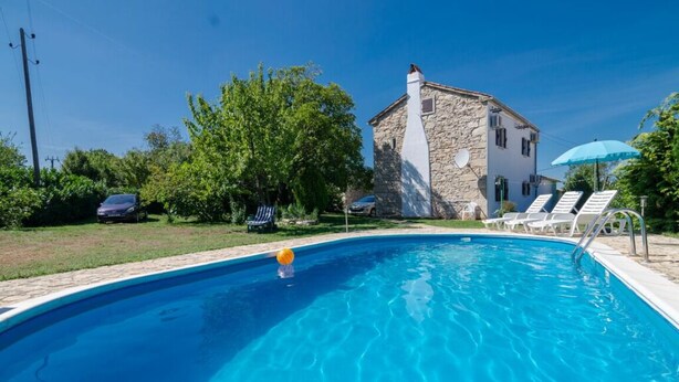 A swimming pool with lounge chairs and an umbrella, surrounded by greenery and a stone building. - Walnut House with a pool (Nedešćina)