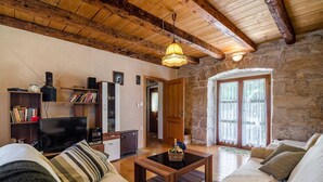 A cozy living room with a wooden ceiling, stone walls, a television, a bookshelf, and a sofa. - Walnut House with a pool (Nedešćina)