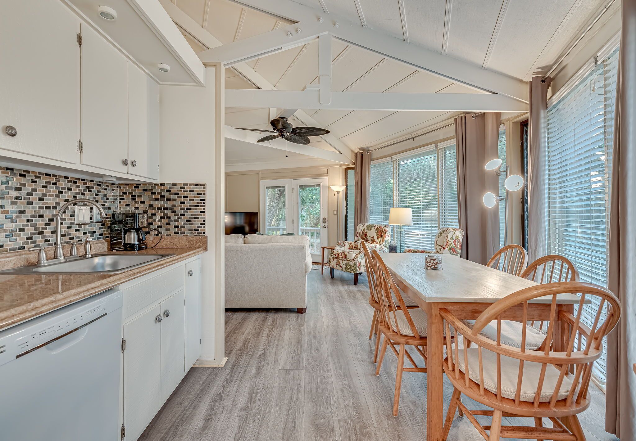 A modern kitchen with white cabinets, a tiled backsplash, and a wooden dining table with chairs.