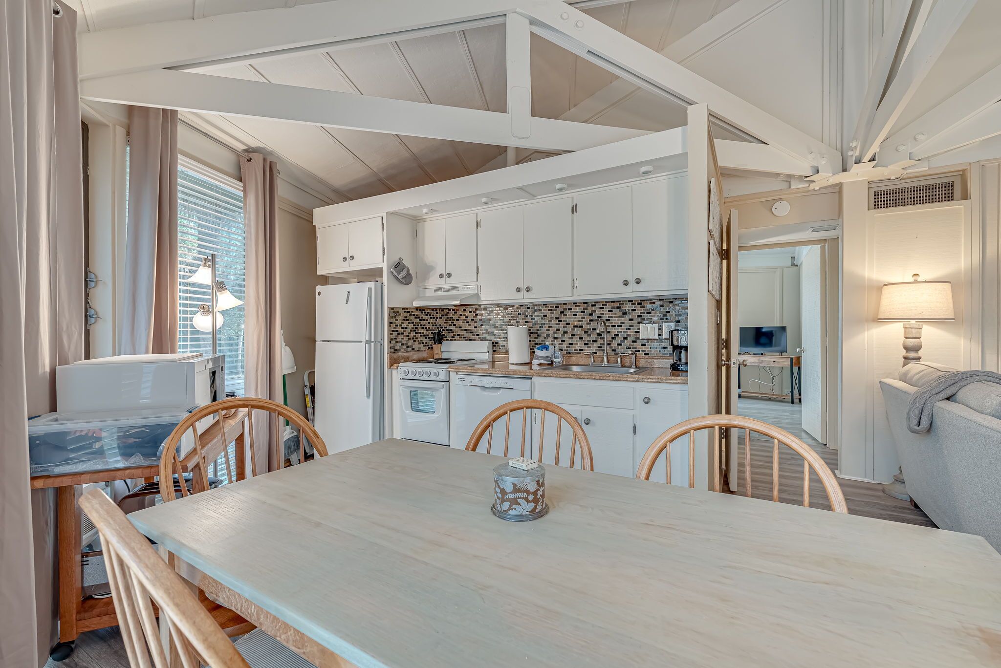 Una cocina moderna con armarios blancos, salpicadero de azulejos y sillas de madera alrededor de una mesa.