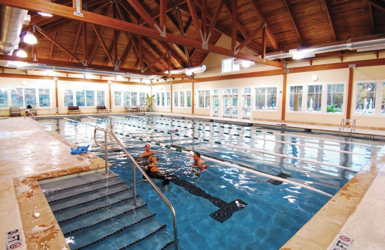 An indoor swimming pool with clear lanes, wooden beams, and large windows.