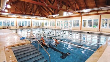 An indoor swimming pool with clear lanes, wooden beams, and large windows.