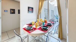 Un coin repas avec une table ronde dressée pour quatre personnes, agrémentée d’assiettes, de couverts et de verres.
