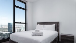 Una habitación de hotel moderna con un ventanal grande, una cama bien hecha y una mesita de noche pequeña.