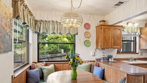 Una cucina accogliente con mobili in legno, un tavolo da pranzo con sedie, un'ampia finestra vista sul verde e un lampadario.