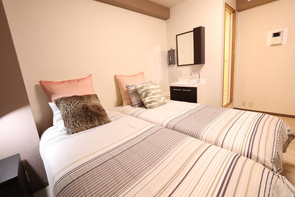 A bedroom with two beds, a bedside table, a mirror, a sink, and a window.