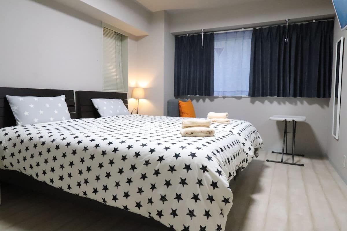 A hotel room with a bed, a nightstand, a window with curtains, and a small table.