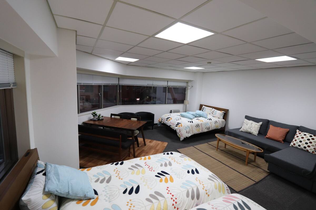 A modern, well-lit room with a bed, sofa, and dining area.