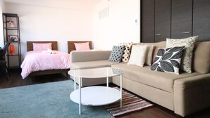 A modern living room with a beige sofa, a round coffee table, and a bed with a pink bedspread. - Residence Osaka Nipponbashi (Osaka)