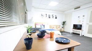Hotellihuone, jossa on sänky, televisio, työpöytä tietokoneella sekä ikkuna, jossa on sälekaihtimet.