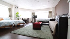 Hotellihuone, jossa on kaksi sänkyä, sohva, televisio, työpöytä ja ruukkukasvi.