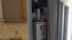 Una cocina con un refrigerador blanco, un microondas y una estantería con productos de limpieza.