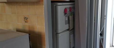 A kitchen with a white refrigerator, a microwave, and a shelf with cleaning supplies.