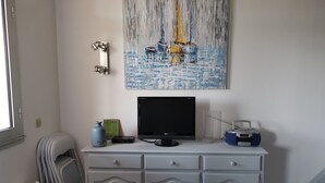 Una habitación con un armario blanco, un cuadro de un velero, un monitor negro y una radio.