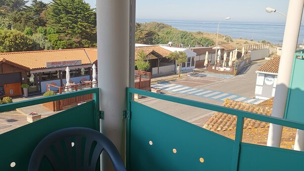 Un balcón con mesa y sillas, con vista a la costa, edificios y el mar.