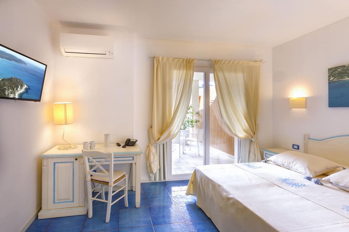 A hotel room with a bed, a desk with a chair, a TV, and a window with curtains.