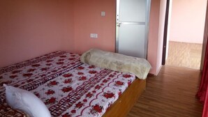 Ein Einzelbett mit einem gemusterten Überwurf, einem weißen Kissen und einer beigen Decke in einem Zimmer mit rosa Wänden und Holzboden.