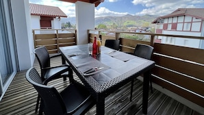 A covered outdoor dining area with a table and chairs, a bottle of juice, and a view of houses and mountains in the background.
