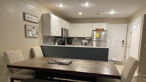 A modern kitchen with white cabinets, a stainless steel refrigerator, and a built-in microwave. There is a dining table with chairs and a bench. - Ledges Complex - Lake front With Slip Included - Beach and 2 Pools (Osage Beach)
