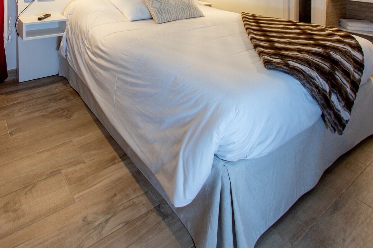 Une chambre d’hôtel moderne avec un grand lit, une table de chevet, une commode et un plancher en bois.