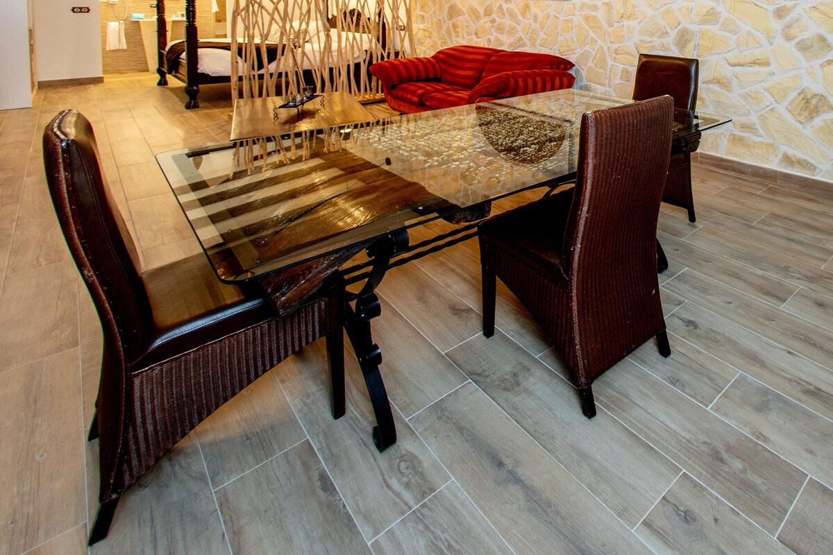 Un coin repas avec une table à plateau en verre, des chaises en bois foncé et un mur en pierre en arrière-plan.